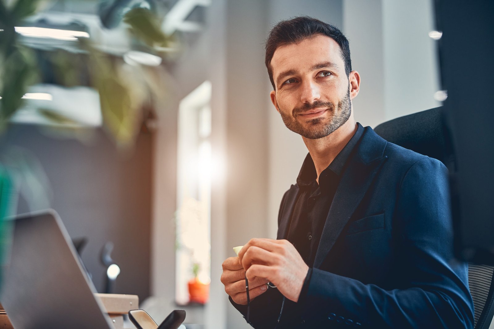 Smiling businessman sitting at workplace with laptop in modern office